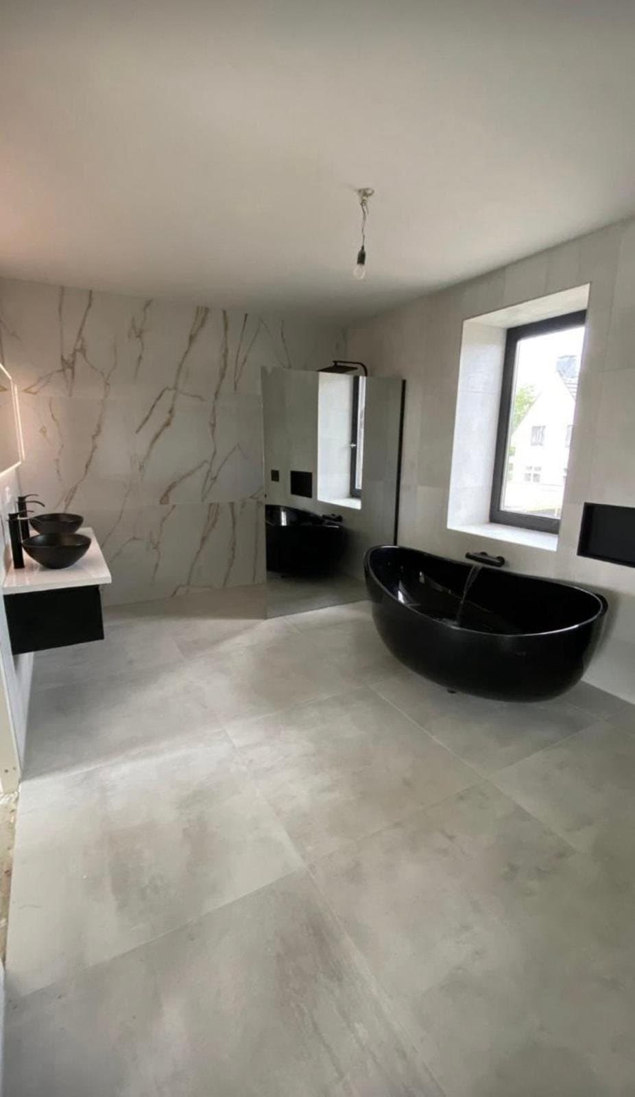 Badkamer met zwart vrijstaand bad en marmerlook tegels